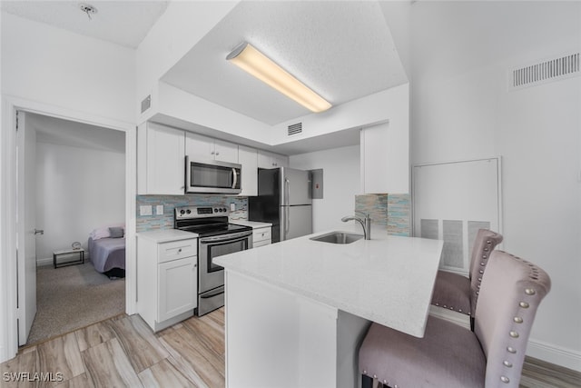 kitchen with sink, decorative backsplash, appliances with stainless steel finishes, a kitchen bar, and white cabinetry