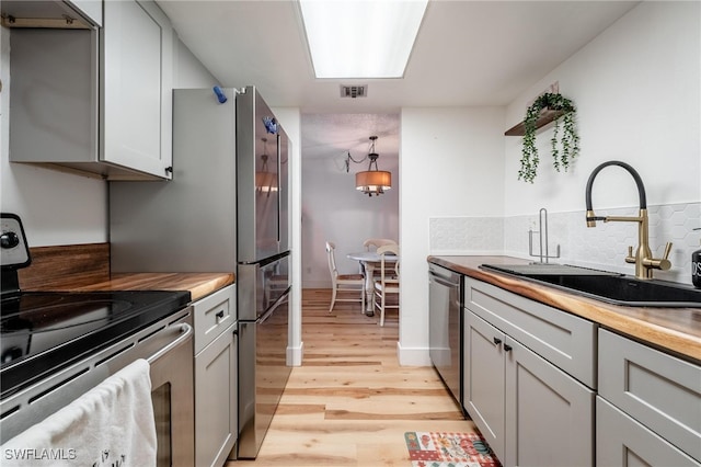 kitchen featuring wooden counters, light hardwood / wood-style floors, stainless steel appliances, decorative light fixtures, and gray cabinets