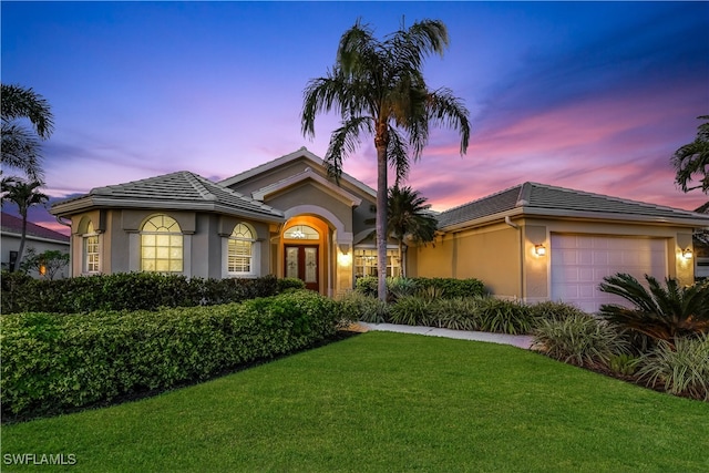 view of front of property with french doors, a garage, and a lawn