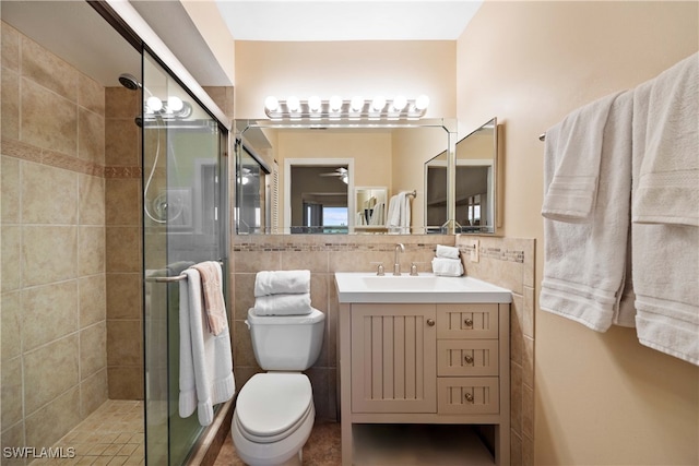 bathroom featuring vanity, ceiling fan, tile walls, toilet, and a shower with shower door