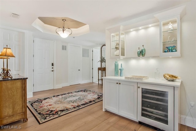 foyer featuring a raised ceiling, light hardwood / wood-style flooring, and beverage cooler