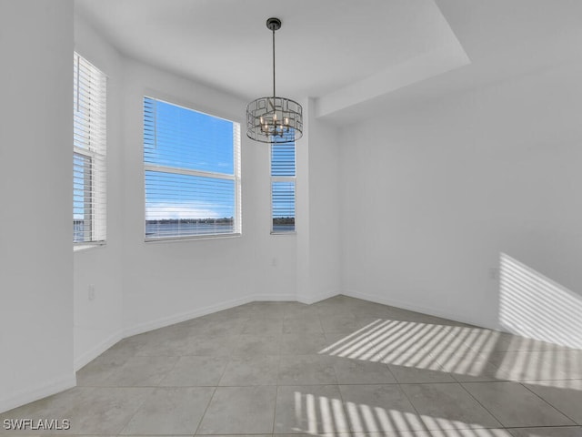 tiled spare room featuring an inviting chandelier