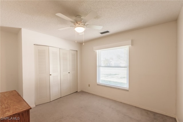 unfurnished bedroom featuring ceiling fan, light colored carpet, a textured ceiling, and a closet