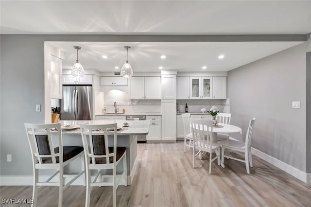 kitchen featuring appliances with stainless steel finishes, light wood-type flooring, decorative light fixtures, and white cabinetry