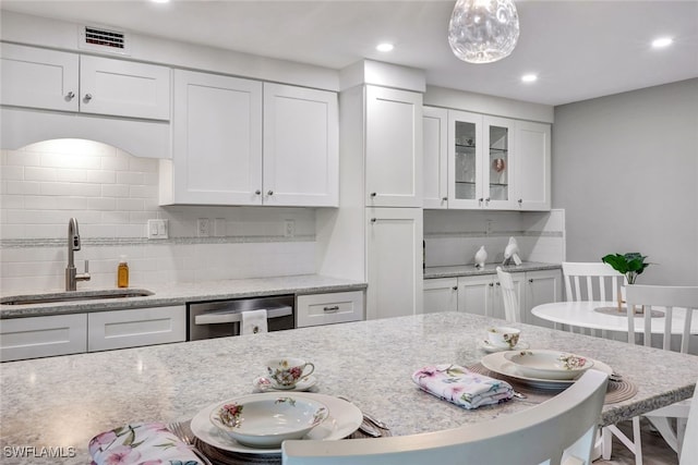 kitchen with tasteful backsplash, stainless steel dishwasher, sink, pendant lighting, and white cabinets