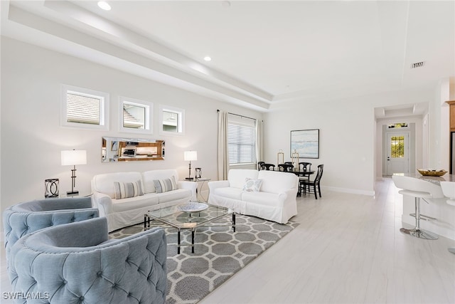 living room featuring a tray ceiling, light hardwood / wood-style flooring, and a healthy amount of sunlight