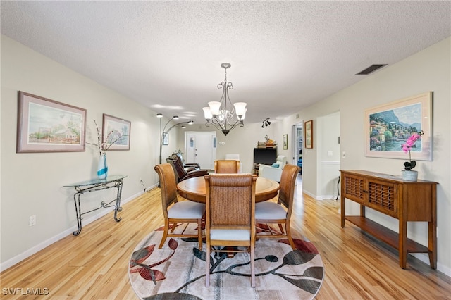 dining space featuring light hardwood / wood-style floors, a textured ceiling, and a notable chandelier