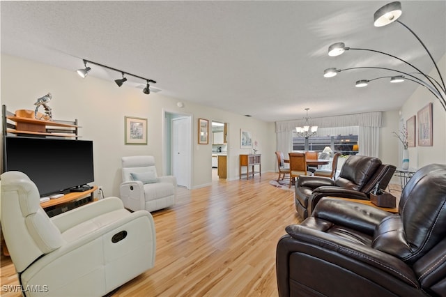 living room with light hardwood / wood-style floors, rail lighting, a textured ceiling, and an inviting chandelier