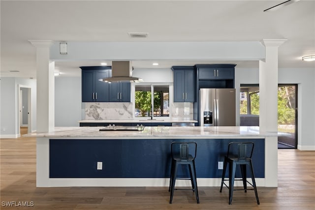 kitchen with stainless steel fridge, a breakfast bar, island range hood, blue cabinetry, and hardwood / wood-style flooring