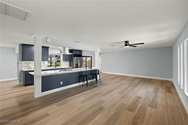 kitchen with a kitchen bar, wall chimney exhaust hood, ceiling fan, light hardwood / wood-style flooring, and a center island