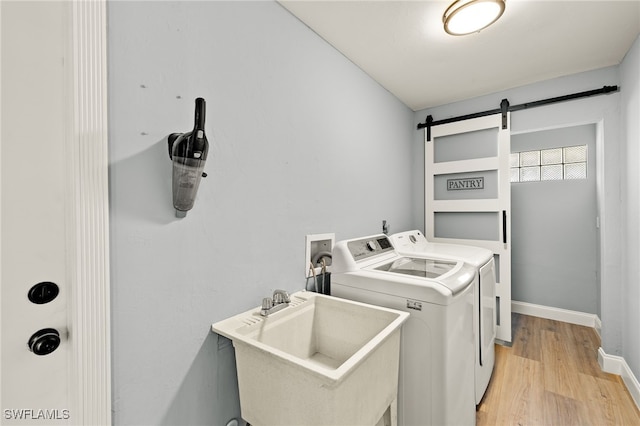 laundry area with independent washer and dryer, a barn door, light hardwood / wood-style flooring, and sink