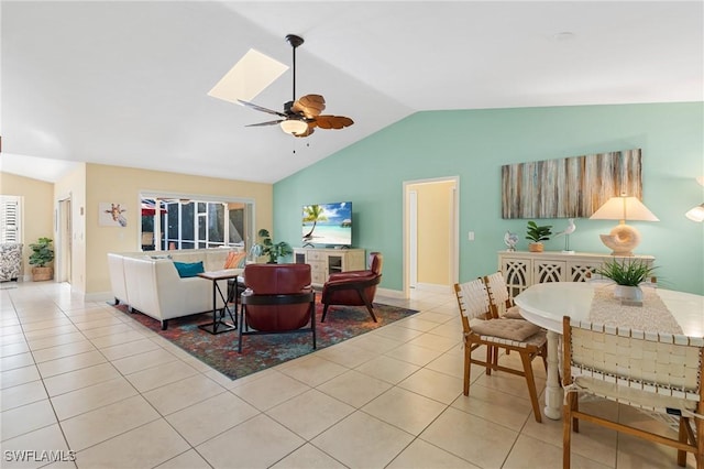 tiled living room featuring lofted ceiling with skylight and ceiling fan