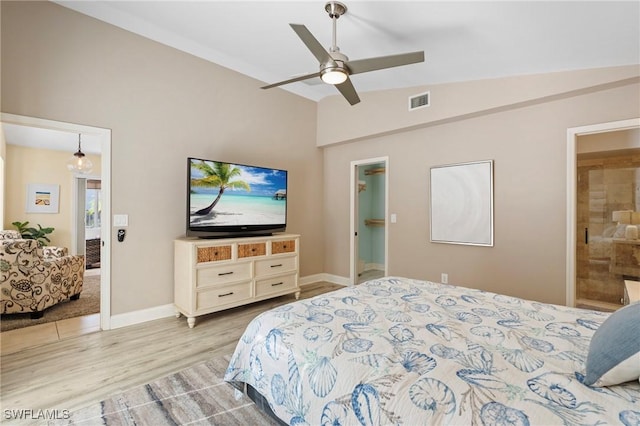 bedroom with lofted ceiling, a walk in closet, ensuite bath, ceiling fan, and light wood-type flooring