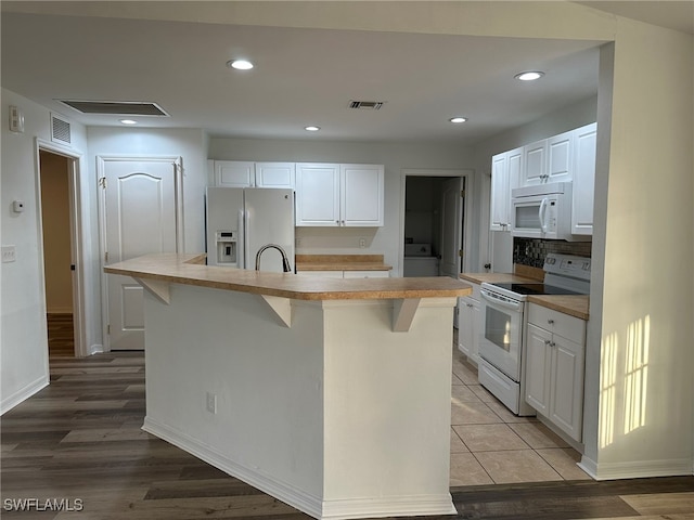 kitchen featuring light hardwood / wood-style flooring, an island with sink, white appliances, a kitchen bar, and white cabinets