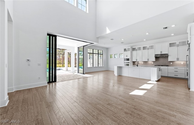 unfurnished living room featuring a healthy amount of sunlight, light wood-type flooring, sink, and a towering ceiling