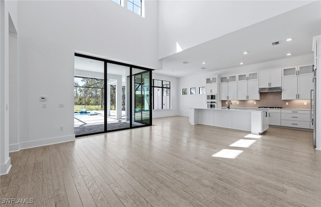 unfurnished living room with light hardwood / wood-style flooring, a healthy amount of sunlight, a high ceiling, and sink