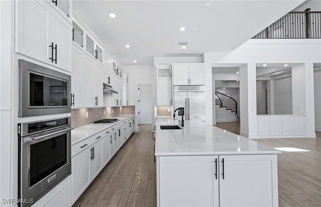 kitchen with appliances with stainless steel finishes, sink, wood-type flooring, a center island with sink, and white cabinetry