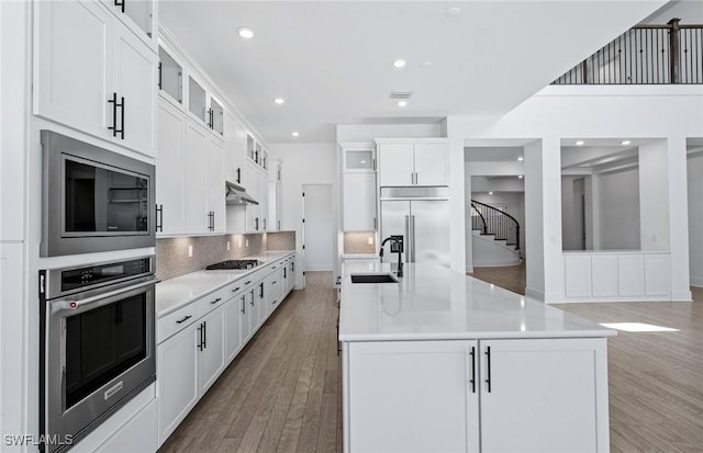 14111 Calaveras Ct, Estero, FL 33928 - kitchen featuring built in appliances, a sink, light wood-type flooring, decorative backsplash, and glass insert cabinets