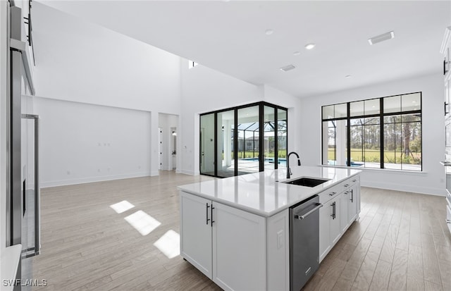 kitchen with a kitchen island with sink, white cabinets, sink, stainless steel dishwasher, and light wood-type flooring