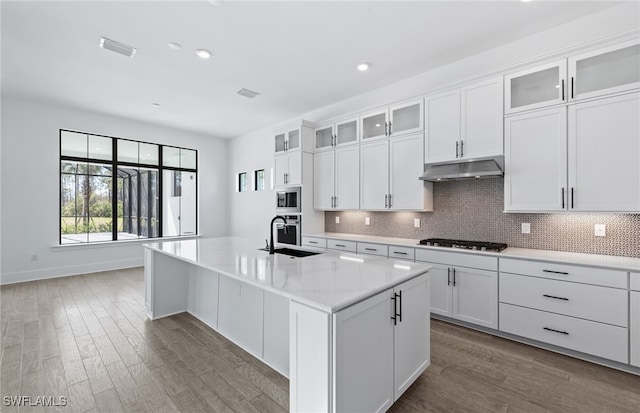 kitchen with dark hardwood / wood-style flooring, an island with sink, decorative backsplash, white cabinets, and appliances with stainless steel finishes