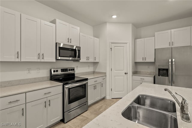 kitchen featuring white cabinets, sink, light stone countertops, light tile patterned floors, and stainless steel appliances