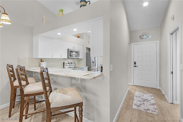 kitchen with a breakfast bar area, appliances with stainless steel finishes, white cabinets, kitchen peninsula, and light wood-type flooring