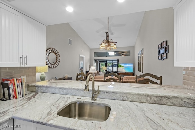 kitchen with light stone counters, white cabinetry, sink, and backsplash