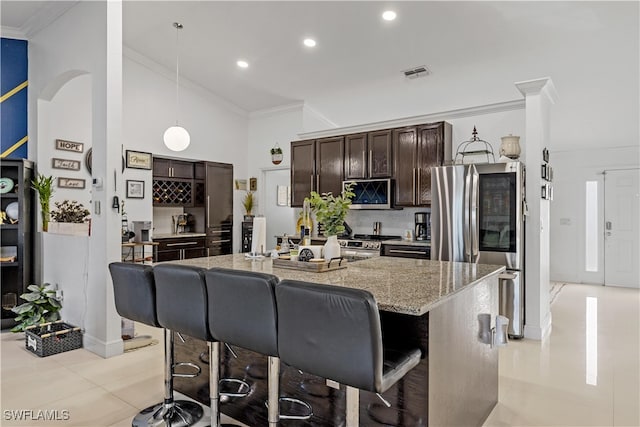 kitchen with hanging light fixtures, appliances with stainless steel finishes, a center island with sink, and dark brown cabinets