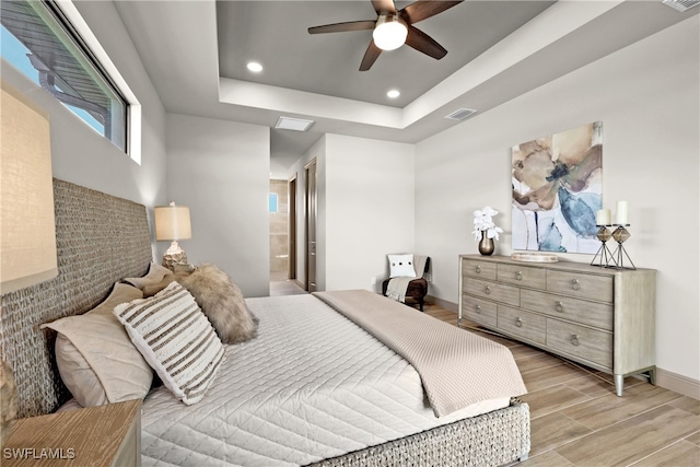 bedroom featuring a tray ceiling, connected bathroom, ceiling fan, and light wood-type flooring