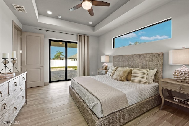 bedroom featuring ceiling fan, light hardwood / wood-style floors, access to outside, and a tray ceiling