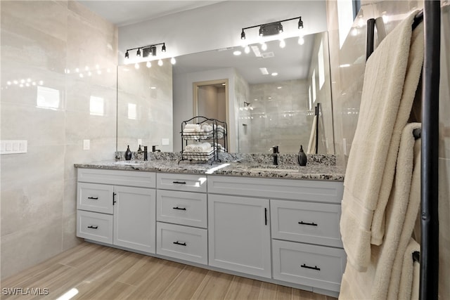 bathroom with a shower, wood-type flooring, vanity, and tile walls