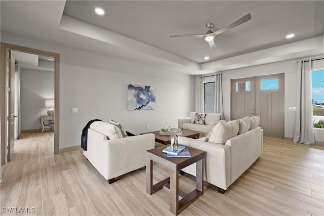 living room with ceiling fan, a raised ceiling, and light wood-type flooring