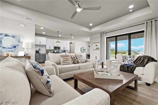 living room with ceiling fan, a raised ceiling, and light hardwood / wood-style flooring