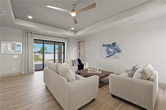 living room featuring ceiling fan, light wood-type flooring, and a tray ceiling