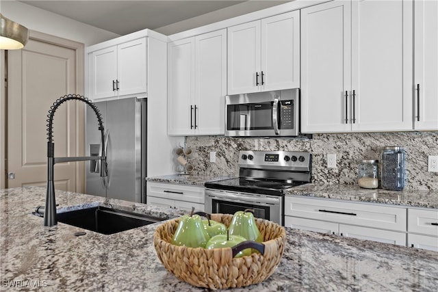 kitchen with light stone countertops, white cabinetry, sink, stainless steel appliances, and backsplash