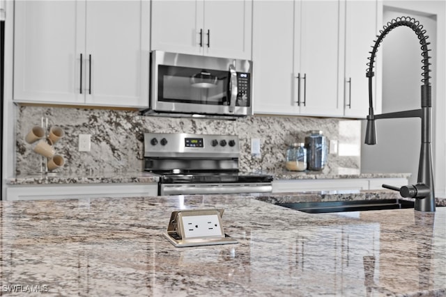 kitchen with light stone countertops, sink, white cabinets, and appliances with stainless steel finishes