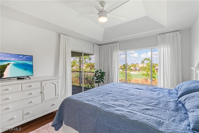 bedroom with access to exterior, a ceiling fan, a raised ceiling, and dark wood-style flooring