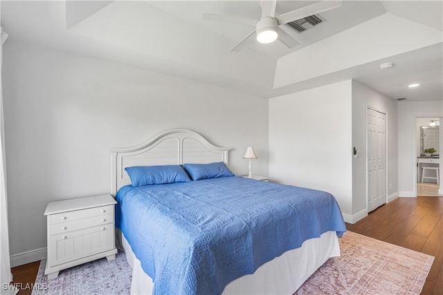 bedroom with a tray ceiling, visible vents, ceiling fan, wood finished floors, and baseboards