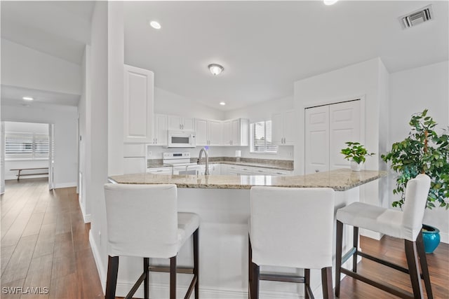 kitchen featuring white appliances, visible vents, white cabinets, a kitchen breakfast bar, and wood finished floors