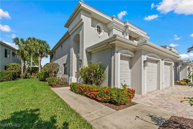 view of side of property featuring an attached garage, decorative driveway, a lawn, and stucco siding