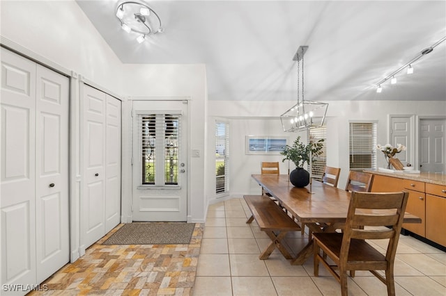 dining area with track lighting, light tile patterned flooring, vaulted ceiling, and a chandelier