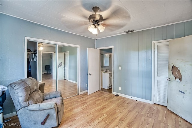 sitting room featuring light wood-type flooring, ceiling fan, crown molding, and wood walls