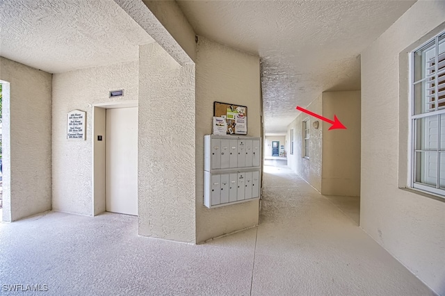 hallway featuring mail boxes, a textured ceiling, and elevator