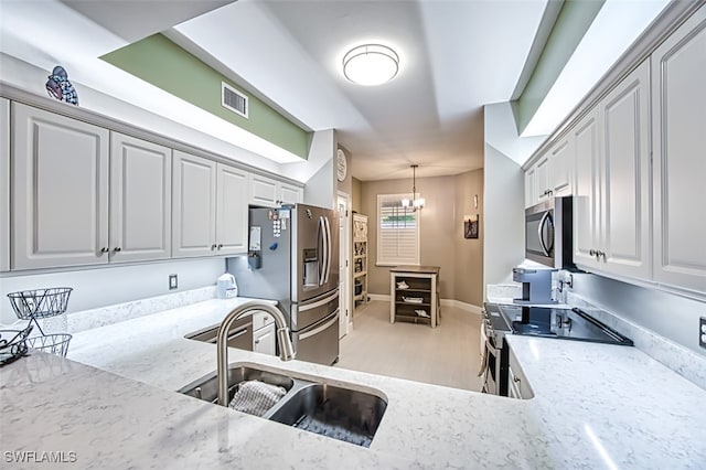 kitchen featuring sink, appliances with stainless steel finishes, decorative light fixtures, light stone counters, and a chandelier