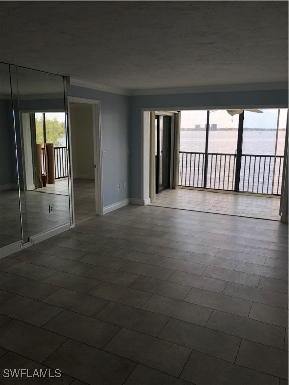 spare room featuring tile patterned floors, crown molding, a water view, and a textured ceiling