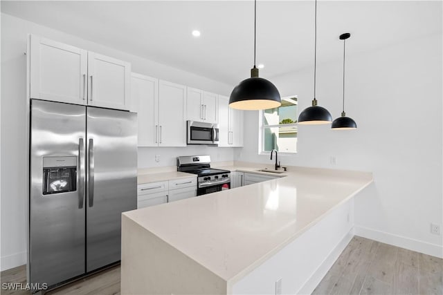 kitchen featuring appliances with stainless steel finishes, light wood-type flooring, sink, pendant lighting, and white cabinetry