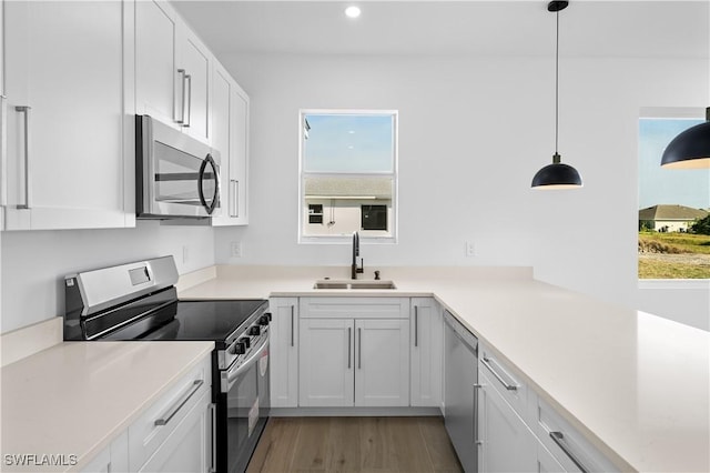 kitchen featuring pendant lighting, sink, light hardwood / wood-style flooring, white cabinetry, and stainless steel appliances