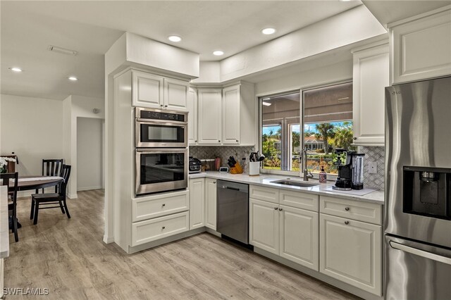 kitchen featuring sink, decorative backsplash, light wood-type flooring, appliances with stainless steel finishes, and white cabinetry