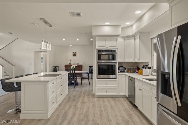 kitchen featuring hanging light fixtures, light wood-type flooring, a kitchen bar, white cabinetry, and stainless steel appliances