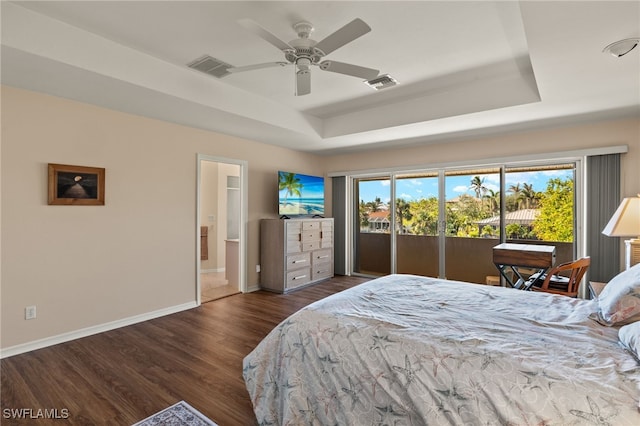 bedroom featuring dark hardwood / wood-style floors, ceiling fan, access to exterior, connected bathroom, and a tray ceiling